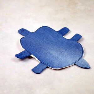 May include: A denim-textured turtle-shaped item with a blue exterior and white trim. The turtle has four flipper-like appendages and a small head. The item is likely a decorative piece or a children's toy.