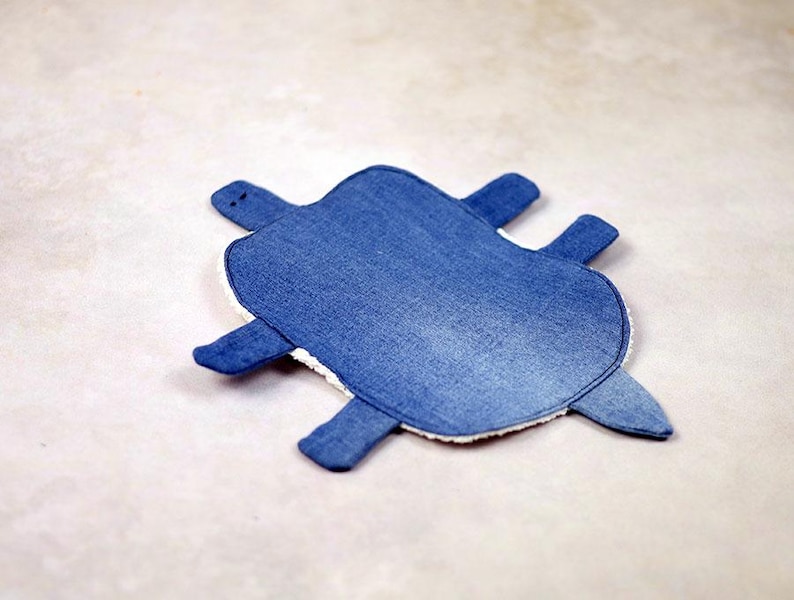 May include: A denim-textured turtle-shaped item with a blue exterior and white trim. The turtle has four flipper-like appendages and a small head. The item is likely a decorative piece or a children's toy.