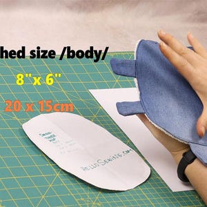 May include: A denim-colored, turtle-shaped item, approximately 8 inches by 6 inches, is held in a hand. A sewing pattern is visible, along with the text "HELLO SEWING.COM" and the dimensions in inches and centimeters.