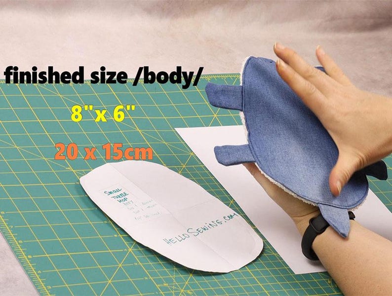 May include: A denim-colored, turtle-shaped item, approximately 8 inches by 6 inches, is held in a hand. A sewing pattern is visible, along with the text "HELLO SEWING.COM" and the dimensions in inches and centimeters.