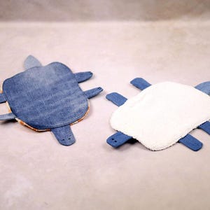 May include: Two handmade turtle-shaped items. One is made of blue denim with orange trim, the other has a white, fluffy top and blue denim legs. These unique items are likely decorative or functional.