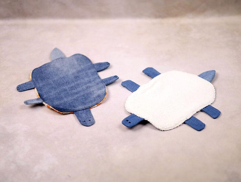 May include: Two handmade turtle-shaped items. One is made of blue denim with orange trim, the other has a white, fluffy top and blue denim legs. These unique items are likely decorative or functional.