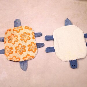 May include: Two handmade turtle-shaped plush toys. One has an orange floral pattern on a cream background, the other is white. Both have denim blue flippers, heads, and tails. These soft toys are likely for children.