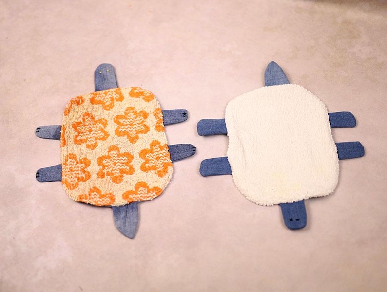 May include: Two handmade turtle-shaped plush toys. One has an orange floral pattern on a cream background, the other is white. Both have denim blue flippers, heads, and tails. These soft toys are likely for children.