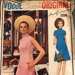 Puede incluir: Un patrón de costura vintage que presenta a dos mujeres con vestidos. La mujer de la izquierda lleva un vestido rosa y un gran sombrero de paja. La mujer de la derecha lleva un vestido azul y guantes blancos. El patrón se titula "Vogue Paris Original" y el número "2206" está impreso en la esquina superior derecha. El texto "Molyneux Original Photographed at Le Grand Vetour in Paris" está impreso en la parte inferior del patrón.
