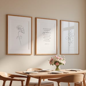 May include: A dining room setting with a light wood table and chairs. Three framed prints with botanical line drawings and inspirational text adorn the wall. A vase of pink and white flowers sits on the table, creating a welcoming atmosphere.