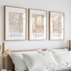 Könnte beinhalten: Ein Schlafzimmer mit einem Bett mit weißer Bettwäsche und Kissen sowie einer beigen Decke. Über dem Bett befinden sich drei gerahmte Drucke mit den Wörtern „SEER“, „TRUST“ und „COME“. Der Raum ist in neutralen Tönen gehalten, mit Tageslicht.