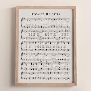 Può includere: Una stampa incorniciata con spartito musicale con il titolo "BECAUSE HE LIVES" in alto. La musica è in inchiostro nero su sfondo color crema. La cornice è di colore legno chiaro. Un vaso decorativo e un piccolo contenitore sono in primo piano.
