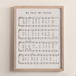 May include: A framed print featuring sheet music with the text "BE THOU MY VISION" at the top. The print has a light wood frame and is displayed against a neutral wall. The sheet music is in black and white.