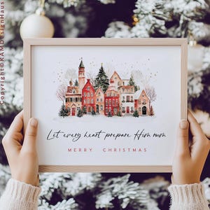 Könnte beinhalten: Ein gerahmter Weihnachtsdruck mit einer Aquarellillustration eines Dorfes mit roten und weißen Gebäuden, Schnee und immergrünen Bäumen. Der Text lautet "Let every heart prepare Him room" und "MERRY CHRISTMAS". Der Rahmen ist hellbraun.