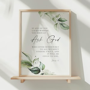 May include: A framed print featuring the words "Ask God" in stylish script, with watercolour-style green foliage. The print includes a quote from James 1:5. The frame is a light wood colour.