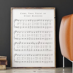 May include: A framed print featuring sheet music with the text "COME, THOU FOUNT OF EVERY BLESSING" at the top. The musical notes and lyrics are printed in black on a white background. The frame is a light brown color.