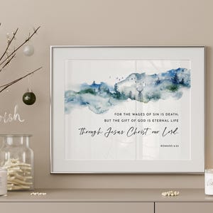Könnte beinhalten: Ein gerahmter Wandkunstdruck mit einer Aquarelllandschaft aus blauen und grünen Bergen und Bäumen. Der Text lautet: For the wages of sin is death, but the gift of God is eternal life through Jesus Christ our Lord. Romans 6:23.