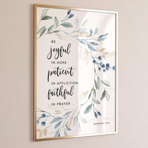Könnte beinhalten: Ein Aquarelldruck mit goldenem Rahmen, der ein florales Design mit blauen und grünen Blättern und Beeren zeigt. Der Druck enthält den Text "Seid fröhlich in der Hoffnung, geduldig in der Bedrängnis, treu im Gebet, Römer 12:12".