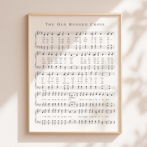 Puede incluir: Una impresión enmarcada con partituras titulada "The Old Rugged Cross" en un marco dorado. La música está impresa en negro sobre un fondo blanco. La impresión se muestra en una pared de color neutro.