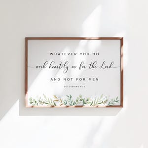 May include: A framed print with a white background and a black text quote: "Whatever you do work heartily as for the Lord and not for men." The quote is from Colossians 3:23. The bottom of the print features a watercolour illustration of green leaves and white flowers.