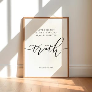 May include: A framed print featuring the words "LOVE DOES NOT DELIGHT IN EVIL BUT REJOICES WITH THE truth" and "1 Corinthians 13:6" in black script. The frame is light brown, and the background is white.