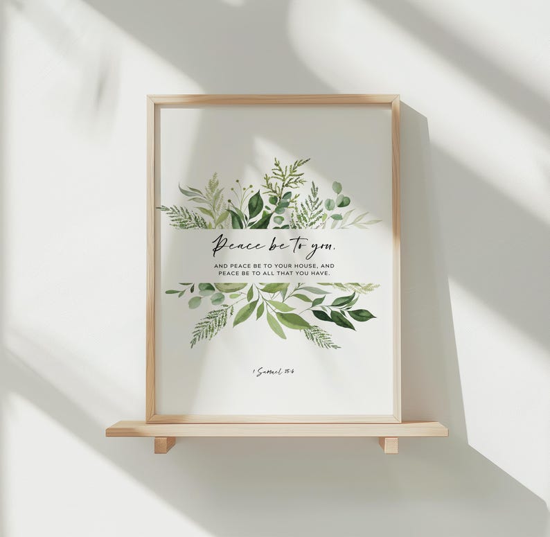 May include: A framed print with the text "Peace be to you." and a botanical design of green leaves. The print is in a light wood frame and rests on a small wooden shelf. The text also includes the phrase "And peace be to your house, and peace be to all that you have."