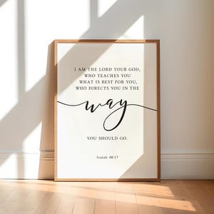 May include: A framed print with a light wood-tone frame. The white background features black text that reads "I AM THE LORD YOUR GOD...YOU SHOULD GO." The word "way" is in a cursive font. The text "Isaiah 48:17" is at the bottom.