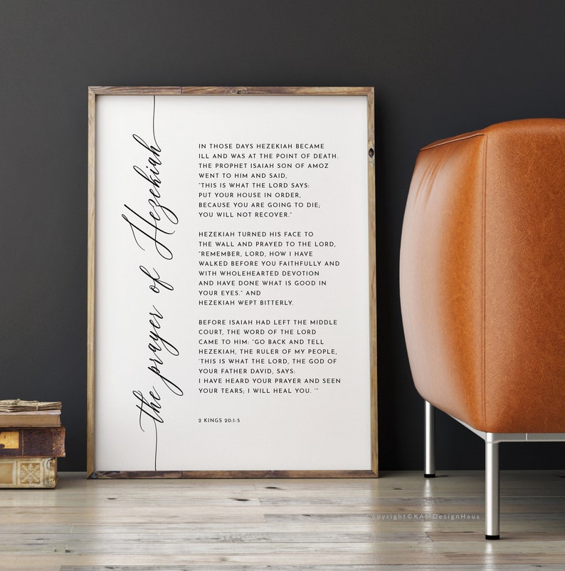 May include: A framed print with the text "The prayer of Hezekiah" in elegant script. The print features a passage from 2 Kings 20:1-5, set against a white background. The frame is a light wood color, and the print is displayed near a leather chair.