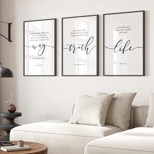 May include: Three framed art prints with black frames and white backgrounds. Each print features elegant black script with inspirational quotes: "way", "truth", and "life". The prints are displayed above a white sofa.