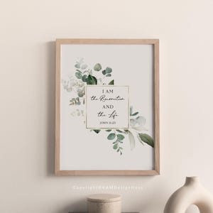 Puede incluir: Una impresi&oacute;n enmarcada con fondo blanco y marco dorado. La impresi&oacute;n presenta una ilustraci&oacute;n de acuarela de hojas de eucalipto y flores blancas. El texto "YO SOY la resurrecci&oacute;n y la vida JUAN 11:25" est&aacute; escrito en letra cursiva negra.