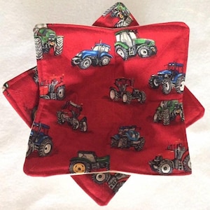 May include: Two red, square-shaped fabric items with a repeating pattern of colorful tractors. The tractors are in various colors, including blue, green, and red, and are set against a solid red background. The items appear to be quilted or padded.