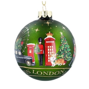 Könnte beinhalten: Grüne Weihnachtskugel mit London-Illustrationen. Zeigt ein schwarzes Taxi, eine rote Telefonzelle, einen königlichen Gardisten, einen Corgi und einen Weihnachtsbaum. Die Worte "ON LONDON" sind unten aufgedruckt. Enthält eine goldfarbene Metallkappe und eine Aufhängeschlaufe.