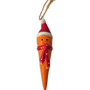 May include: A novelty carrot Christmas ornament. The orange carrot has a smiling face, a red Santa hat with white trim, and a red scarf with white polka dots. A natural twine loop is attached for hanging. Festive holiday decoration.