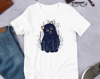 May include: White t-shirt with a black cat illustration surrounded by gold floral details. The cat is looking to the right and has a playful expression.