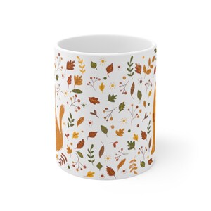 May include: White ceramic mug with a pattern of orange, yellow, and green leaves, berries, and flowers. The pattern is repeated all over the mug.