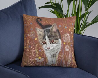 以下が含まれることがあります： 花畑の中を歩くトラ猫のイラストが描かれたクッション。背景は暖色系の茶色で、ピンク、黄色、青色の様々な花や植物が描かれています。