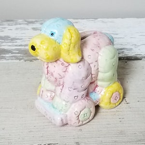 May include: A ceramic piggy bank shaped like a patchwork dog with blue, yellow, pink, and green colors. The dog has a black nose and blue eyes.