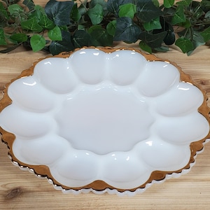 May include: White milk glass egg plate with a gold rim and scalloped edge. The plate has 12 individual indentations for serving eggs.