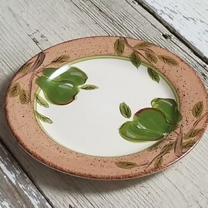May include: A round, white ceramic plate with a brown rim and green pears painted on it. The pears are on branches with green leaves.