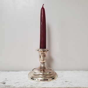 May include: A silver candlestick with a burgundy candle on a white surface.