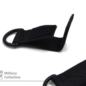 Może przedstawiać: Czarny pasek nylonowy z metalowym pierścieniem i hakiem. Pasek ma zapięcie na rzep, a na pasku nadrukowany jest napis "Military Collection".