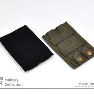Peut inclure: Deux morceaux de tissu avec du velcro. L'un est noir et l'autre est vert olive avec un motif en grille et deux boutons en laiton. Le texte "Velcro Patch Panel Handcraft of Modern Evolution" est imprimé sous le tissu.