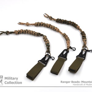 May include: Three green and brown camouflage paracord keychains with black metal clips. The keychains are labelled "Ranger Beads: Mountain Camo Handcraft of Modern Evolution".