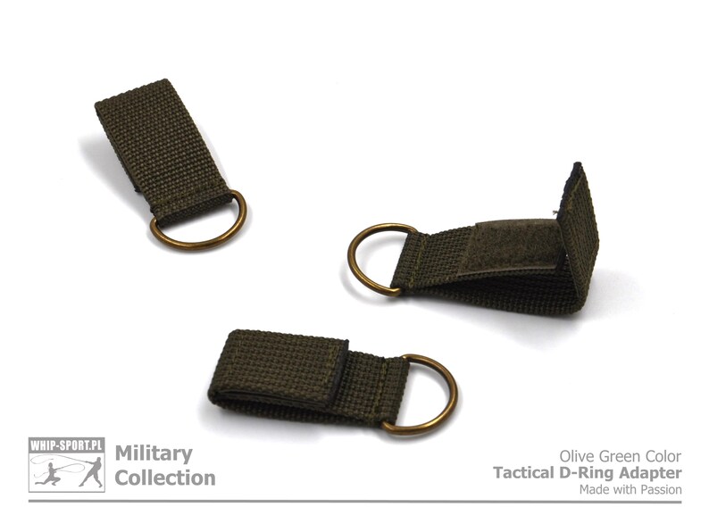 Pode incluir: Adaptador de anel D t&aacute;tico de cor verde oliva com fecho de velcro. O adaptador &eacute; feito de fita de nylon e tem um anel D de lat&atilde;o.  "Olive Green Color Tactical D-Ring Adapter Made with Passion" est&aacute; impresso no fundo branco.