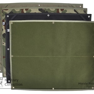 May include: A green, black and camouflage fabric patch panel with metal eyelets. The panel is labelled "Morale Patch Panel Made with Passion".