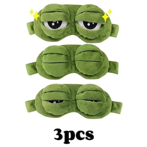 Puede incluir: Tres antifaces verdes con dise&ntilde;o de rana de dibujos animados. Cada antifaz tiene una correa y est&aacute; hecho de material suave. El texto "3pcs" est&aacute; en la parte inferior de la imagen.
