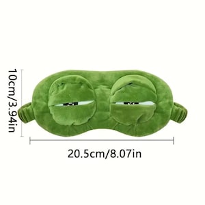 Puede incluir: Una m&aacute;scara para dormir de felpa verde con forma de cara de rana. La m&aacute;scara mide 20,5 cm de largo y 10 cm de alto. Tiene dos ojos grandes y cerrados y est&aacute; dise&ntilde;ada para bloquear la luz para dormir. La m&aacute;scara tiene un aspecto suave y texturizado.