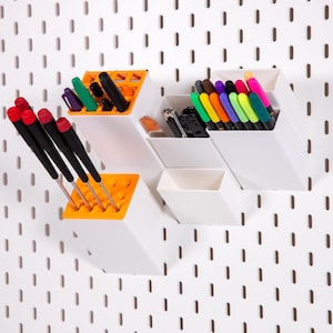 May include: White and orange modular organiser with various tools and writing utensils. The organiser is mounted on a white pegboard. The tools include screwdrivers with red handles and pens in multiple colours.