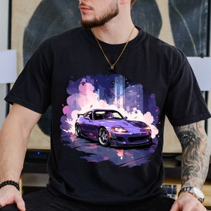 May include: A black t-shirt featuring an illustration of a purple car. The car is driving through a city with smoke coming from the tyres. The car has a driver with purple hair.