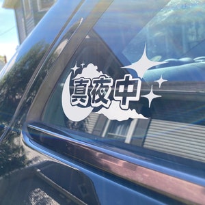 Puede incluir: Una pegatina de vinilo blanco con los caracteres chinos "真夜中" (pronunciado "Shin'ya-chuu") que significa "medianoche" en forma de nube con estrellas a ambos lados, aplicada a una ventana de coche negro.