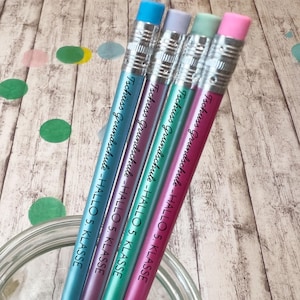 Könnte beinhalten: Vier Bleistifte in Blau, Lila, Türkis und Pink, jeweils mit einem passenden Radiergummi und einer silbernen Metallzwinge. Der Text "Tschüss Grundschule - HALLO 5. KLASSE" ist in Schwarz auf den Schaft jedes Stifts gedruckt.