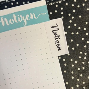 Könnte beinhalten: Ein weißes Notizbuch mit einer blauen Kopfzeile, auf der "Notizen" steht, und einem weißen Aufkleber an der Seite, auf dem ebenfalls "Notizen" steht.
