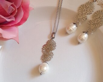 May include: A white porcelain plate with a gold trim design features a delicate silver necklace and earrings with pearl accents. The necklace and earrings have a floral design.