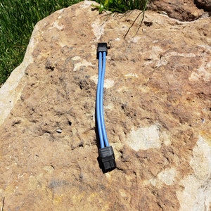 May include: A blue cable splitter with two black connectors. The cable is lying on a brown rock.